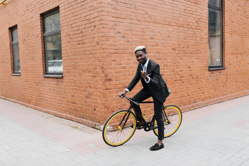 Business on wheels. Stylish confident african businessman pointed on you ride with his bicycle at building brick wall, copy space