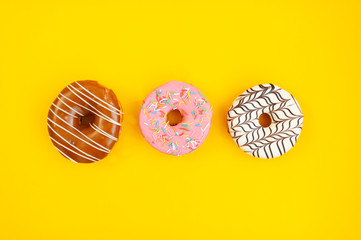 three multi-colored donuts on yellow background, Top view. Copy space 