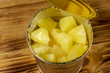 Opened tin can of pineapple pieces on wooden table