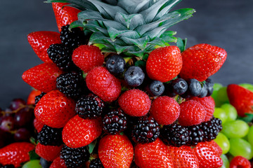 Top view of healthy berries in rainbow colours, pineapple, blackberries, blueberries and raspberries with mint on the off black table, Flat lay