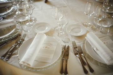 Wedding table setting. White plates and napkins lie on the dinner table decorated with greenery and golden roses