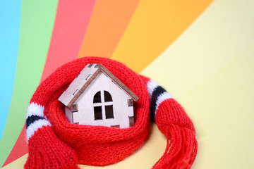 Wooden toy house with windows in a red scarf on a rainbow colored background, warm house, insulation of houses, closeup