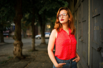 Attractive redhaired woman in eyeglasses, wear on red blouse and jeans skirt posing.