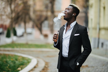Handsome afro american business man with e-cigarette with smoke cloude standing on the city street...