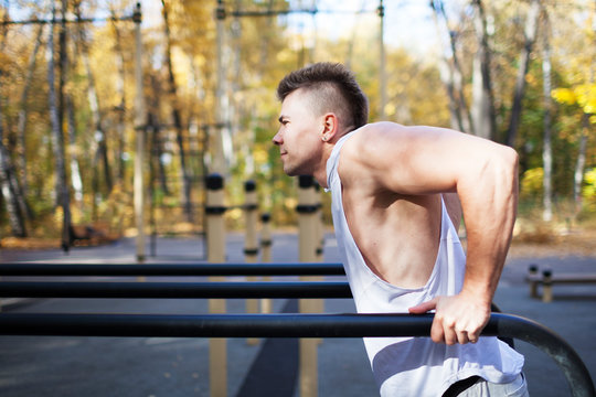Fit man doing triceps dips on parallel bars at park exercising outdoors