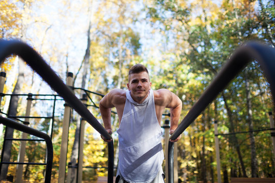 Fit man doing triceps dips on parallel bars at park exercising outdoors