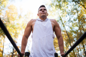 Fit man doing triceps dips on parallel bars at park exercising outdoors