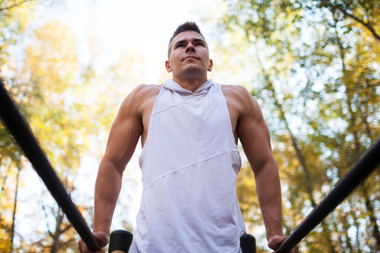 Fit man doing triceps dips on parallel bars at park exercising outdoors