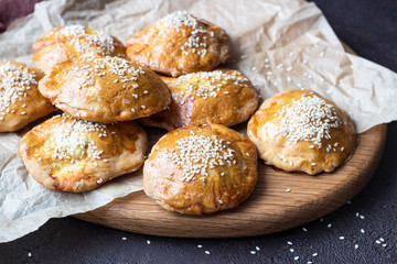 Fresh meat mini pies on a paper on a old dark brown background, rustic style. Fresh baked pasties filled with meat (chicken or turkey). Copy space.