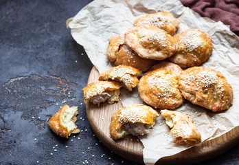 Fresh meat mini pies on a paper on a old dark brown background, rustic style. Fresh baked pasties filled with meat (chicken or turkey). Copy space.