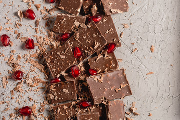 Broken chocolate pieces and chocolate powder, chocolate with hazelnut, chocolate and red pomegranate on beton background with copy paste place