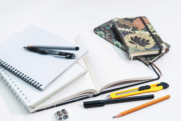 Stack of notebooks and sketchbooks, pencils and pens on a white background