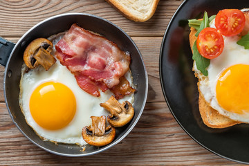 Clouse up top view of fried eggs on black plate and pan with fork, mushrooms and rukkola.