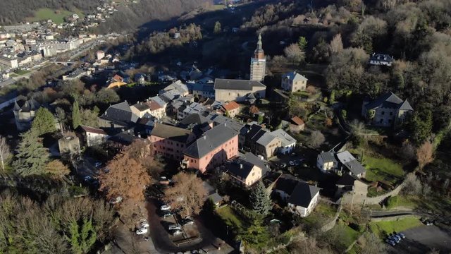Drone shot over looking the medieval city of Conflans, in the French Alps , focus on the church of the village, in the middle of the mountains, on a sunny day. Drone is going forward over the village.