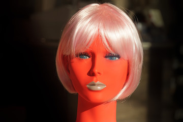 Red head of a mannequin with a strong make-up and a pink wig