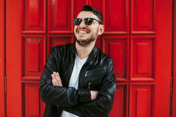 Image of cheerful young man smiling and posing over red door.