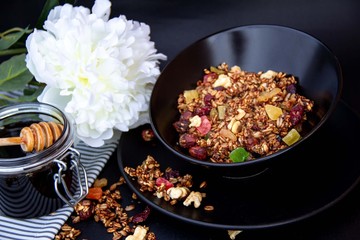 Granola with nuts, berries and honey in black plate.