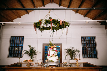 Delicious white wedding cake decorated with flowers stands in the middle of dinner table