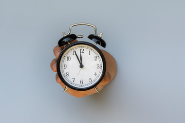 mans hand with an alarm clock set at 5 to 12, just before high noon, symbolic image for action in a crisis