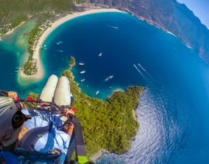 Paraglider tandem flying over the sea with blue water and mountains in bright sunny day. Aerial view of paraglider and Blue Lagoon in Oludeniz, Turkey. Extreme sport. Landscape