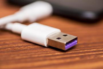 Smartphone with USB cable on the wooden table. Smartphone or tablet with USB cable prepared for data transfer or battery charging