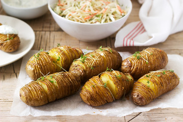 Vegetarian food, hasselback potatoes with sauce and coleslav on a wooden background. Rustic style.