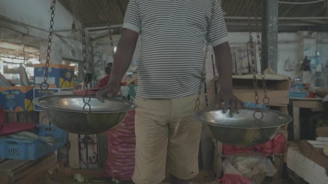 Close up of a mans body in an Indian market place fruit and vegetable stall with large old style scales with two metal bowls to weigh produce