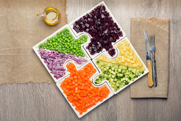 Raw vegetables carrots, peas, onions, cucumber, potatoes, beets cut into cubes lie on puzzles in the form of puzzles and gather in a single large dish.