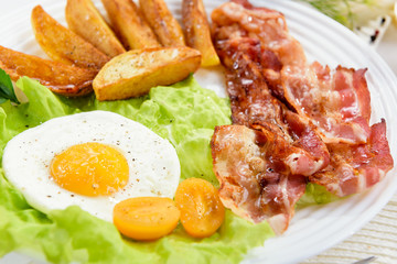 Fried bacon with French fries and a delicate egg, close-up.