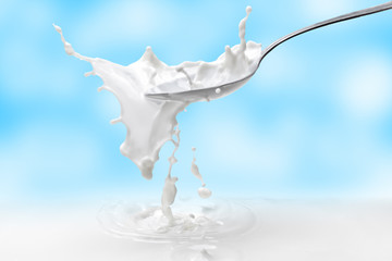 Obraz na płótnie Canvas Milk splash in a spoon with milk against the blue sky with clouds.Beautiful splash of milk on the background of gentle clouds.