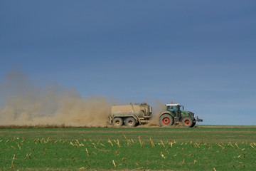 Fototapeta premium tractor with trailer drives across the field and stirs up a lot of dust