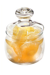 Dried pineapple candy rings, in powdered sugar, close-up under sunlight, lying in a transparent glass jar, on a white background.