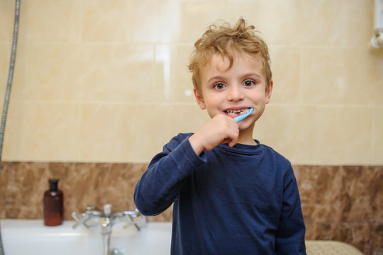 close up photo of a blond boy in blue T-shirt cleaning his teeth in a bathroom