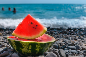 Rest by the sea. Sliced, juicy watermelon on pebble beach, off the coast of the blue ocean..