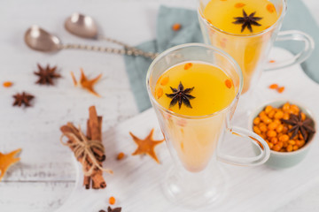 Two high glasses with colorful hot sea buckthorn tea with cinnamon sticks, anise stars and fresh sea buckthorn berries