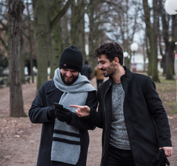 two young guys friends with beards look at the phone while walking in a park
