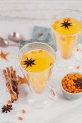 Two high glasses with colorful hot sea buckthorn tea with cinnamon sticks, anise stars and fresh sea buckthorn berries