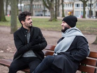 two young boys with beards sitting on a bench having a pleasant conversation, gay couple enjoying time together