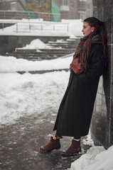 stylish photograph of a portrait of an attractive woman with long pigtails, dressed in an eco-coat and scarf, walked in a winter-frozen city