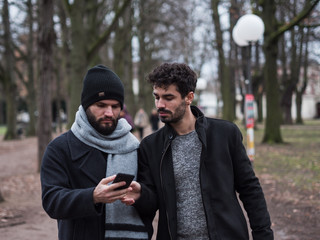 two young guys friends with beards look at the phone while walking in a park