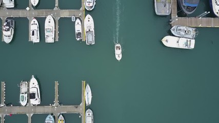 Aerial birds eye view flying over a boat harbor in Homer, Alaska, with boats docked at the jetty and one leaving the port