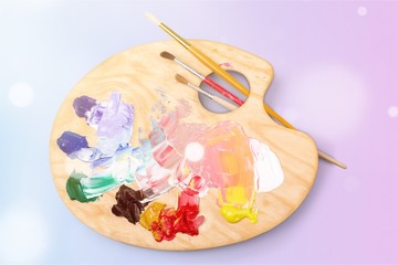 Wooden art palette with blobs of paint and a brushes on white