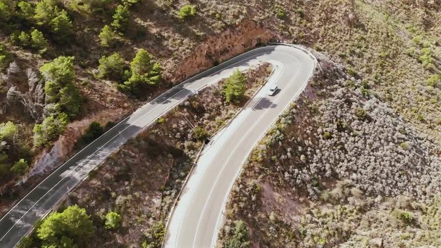Aerial view of car driving on country road in forest. Cinematic drone shot flying over road in pine tree forest in Spain