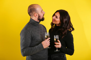 Young sexy model couple with glasses on champagne on yellow background 