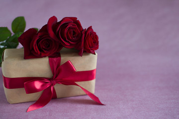 box tied with red ribbon, three red roses on pink background (horizontally, close up)