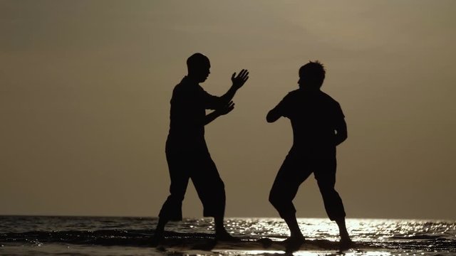 Martial artists friendly sparring on the beach at sunset in slow motion, 50 fps.