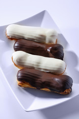 French dessert Eclair with white and black chocolate on white plate. Closeup. Selective focus. High key.