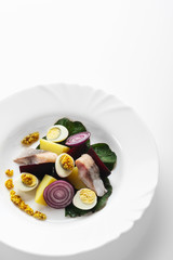 Salad from salty herring, beet, boiled potatoes, quail eggs and onions. With french mustard. High Key. Selective focus.