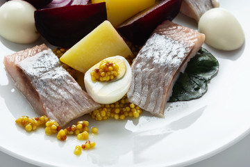 Salad from salty herring, beet, boiled potatoes, quail eggs and onions. With french mustard. High Key. Selective focus.