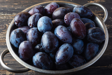 Closeup of fresh juicy plums in a metal bowl on wooden rustic background. Vegan diet. Selective focus.